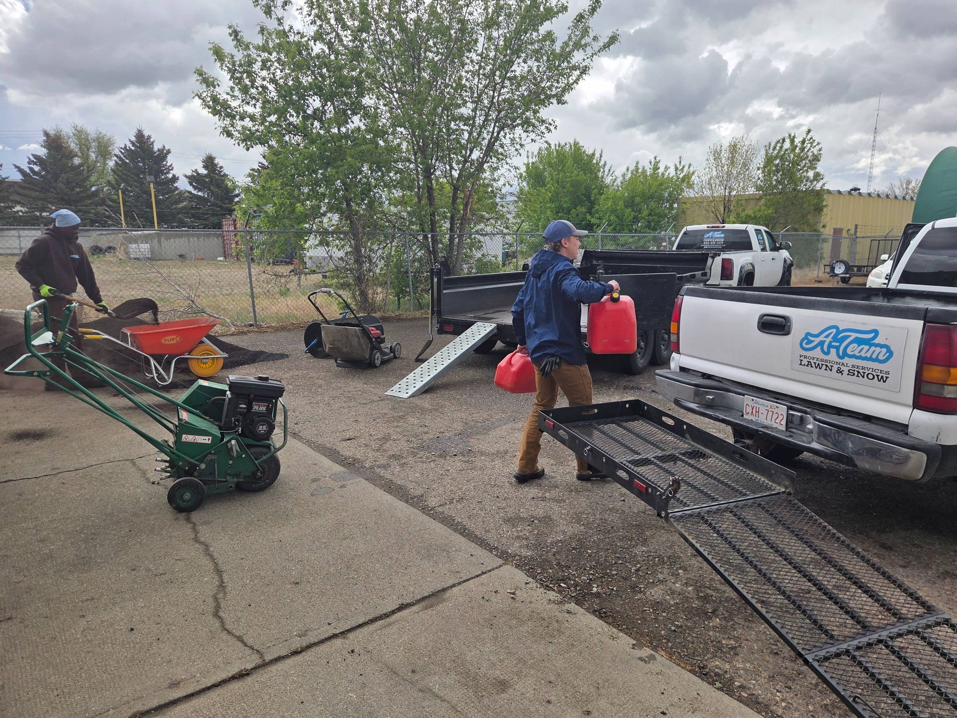 Workers loading equipment into a pickup truck in a driveway, with ramps and landscaping tools nearby