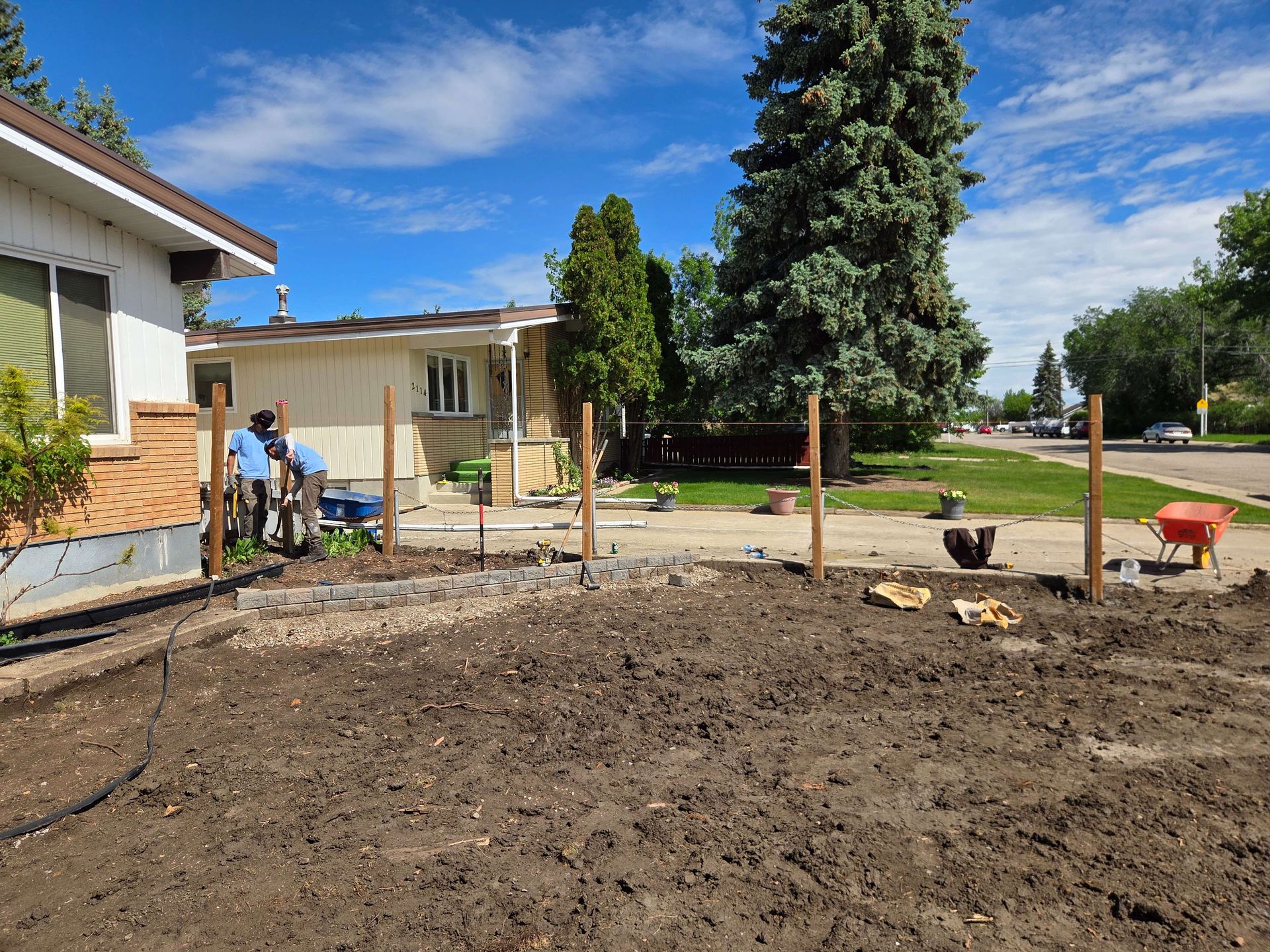 Backyard with freshly tilled soil, small shed, and two people working near the house