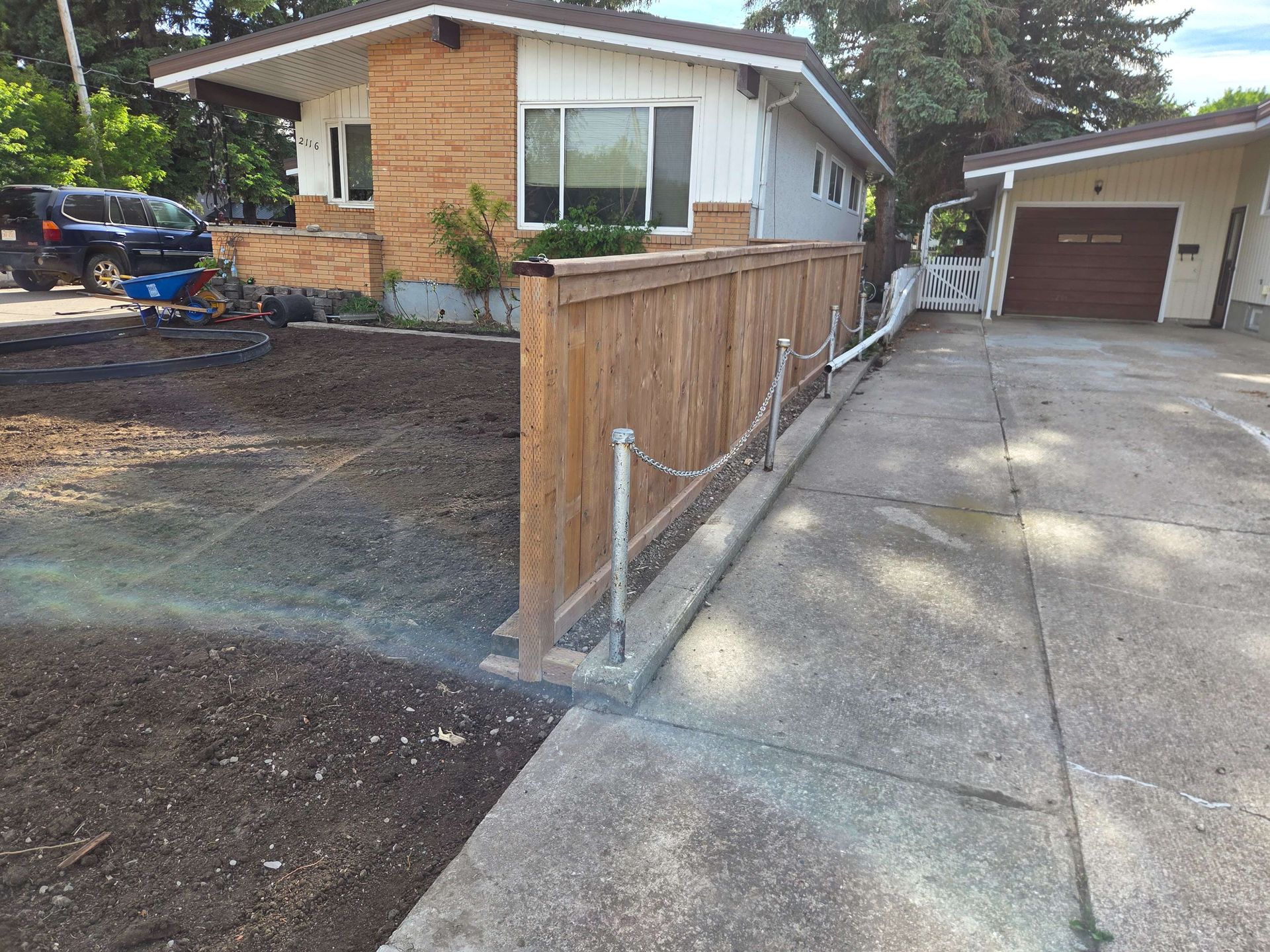 Residential driveway beside a brick house with a wooden fence and garage, showing construction work in progress