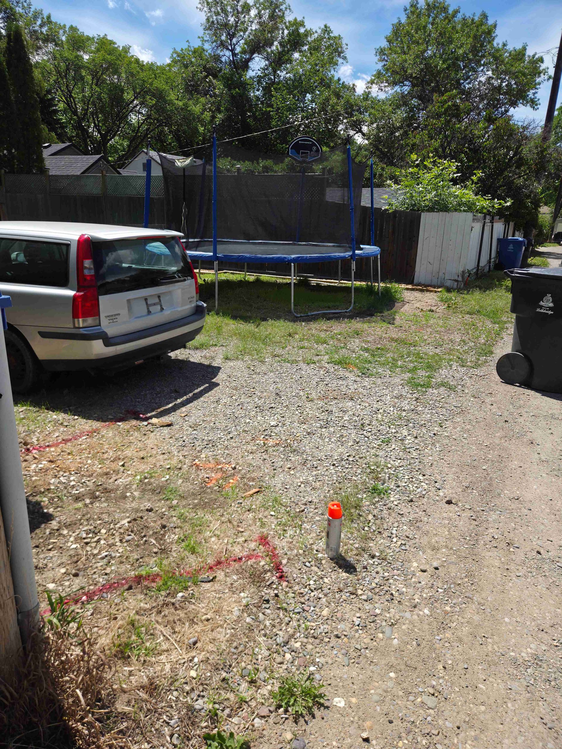 Gravel driveway with parked white van, trampoline, and trees in a backyard under bright sun