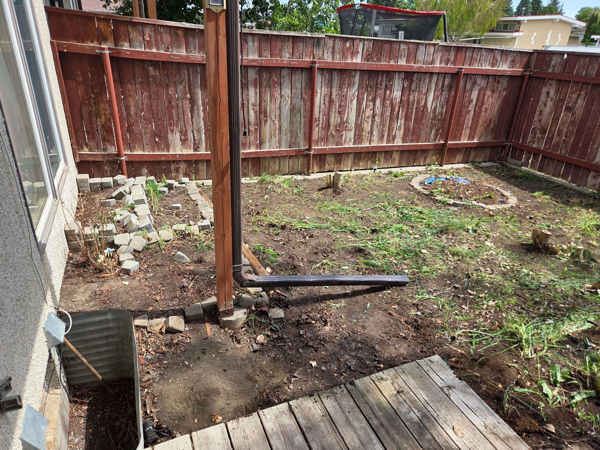 Backyard with bare dirt, a wooden fence, and a red rusted metal post near a patio edge