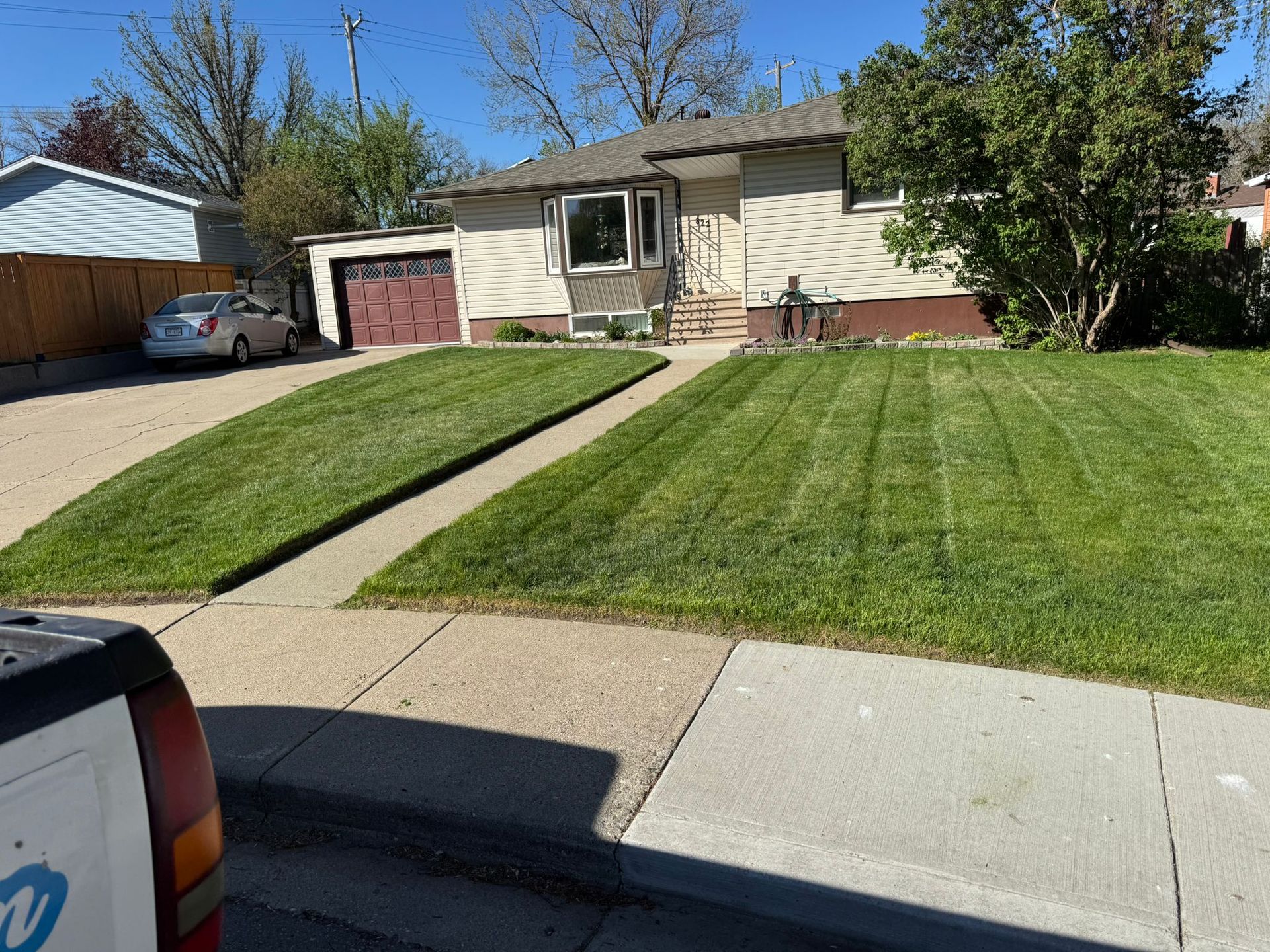 Suburban house with a green lawn, driveway, garage, and sidewalk under a clear blue sky