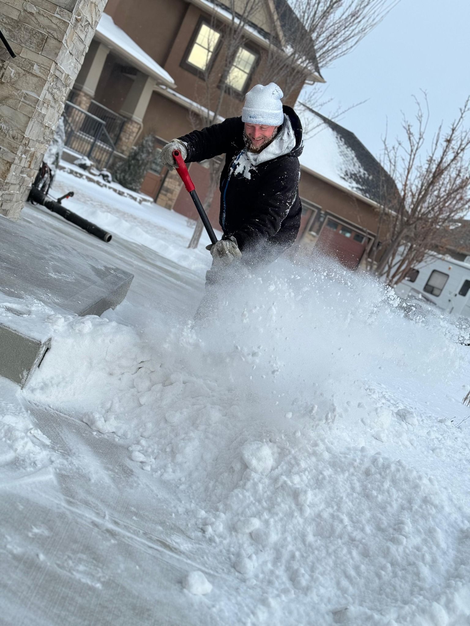 A person shovels snow off a driveway in front of a house on a winter day. A person shovels snow off a driveway in front of a house on a winter day.