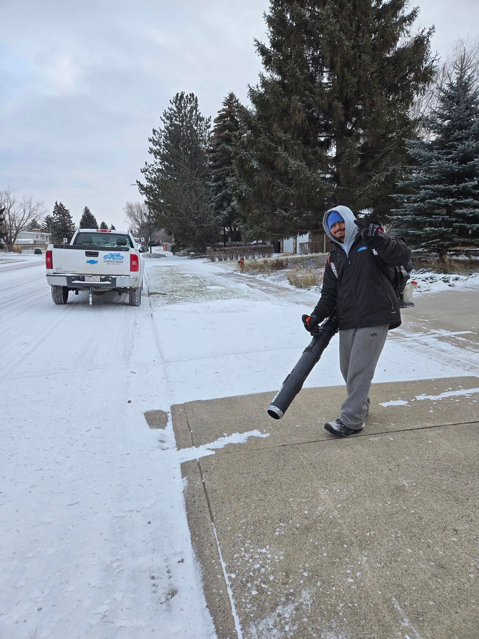A person uses a backpack leaf blower to clear light snow from a paved driveway.
