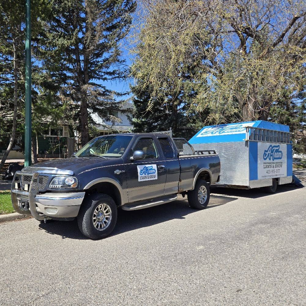 A dark-colored pickup truck parked on a residential street, towing a large, blue and white utility trailer.