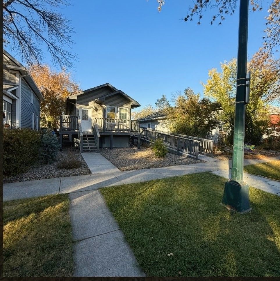 Residential walkway and stairs leading to a gray house, with a grassy yard and autumn trees under a blue sky