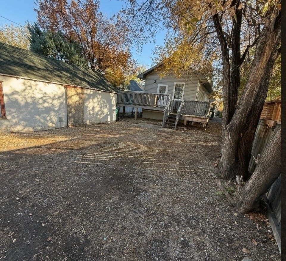 Gravel backyard with two trees, a white garage, and a small deck beside a gray house.