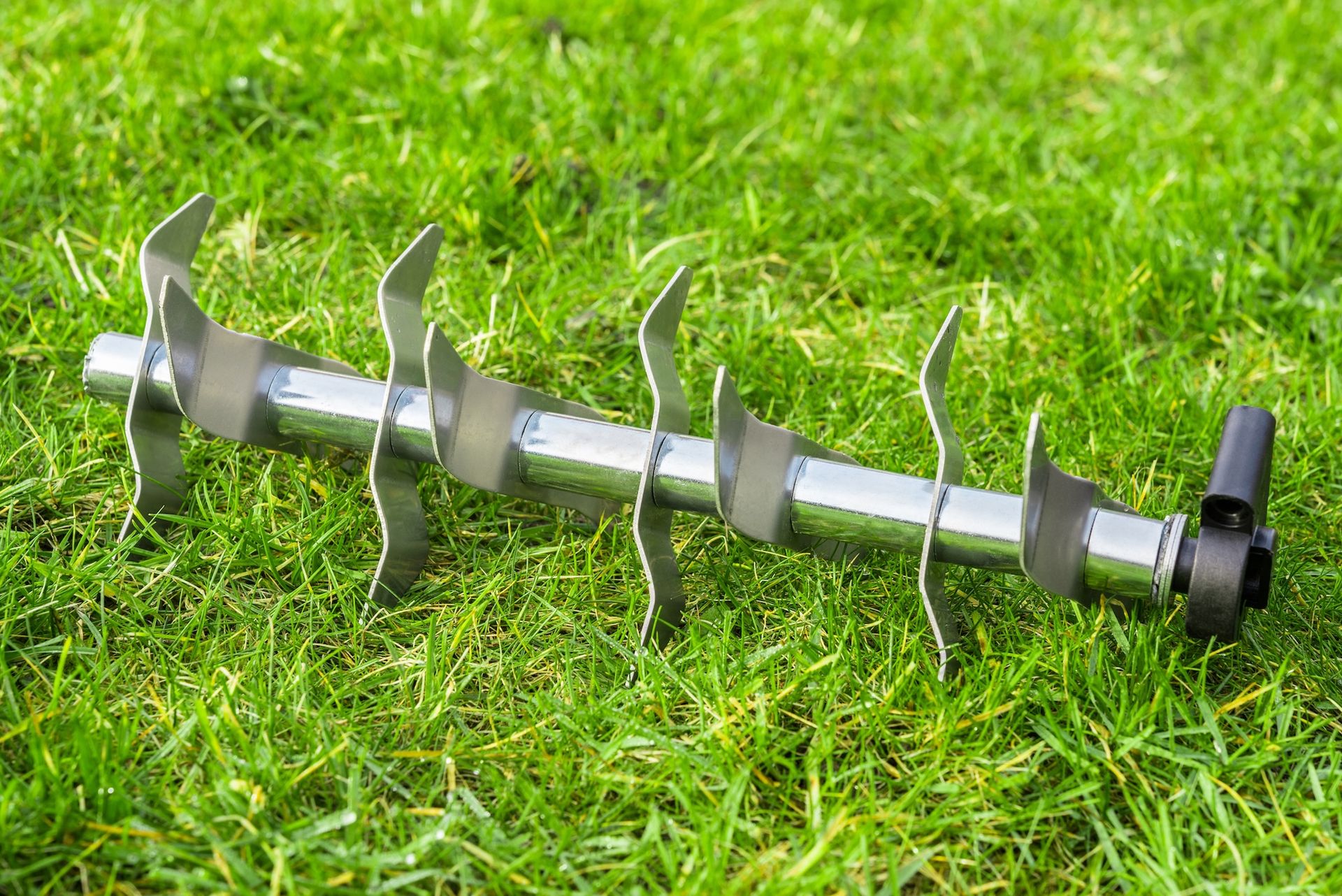 A silver aerator or dethatcher blade on green grass.