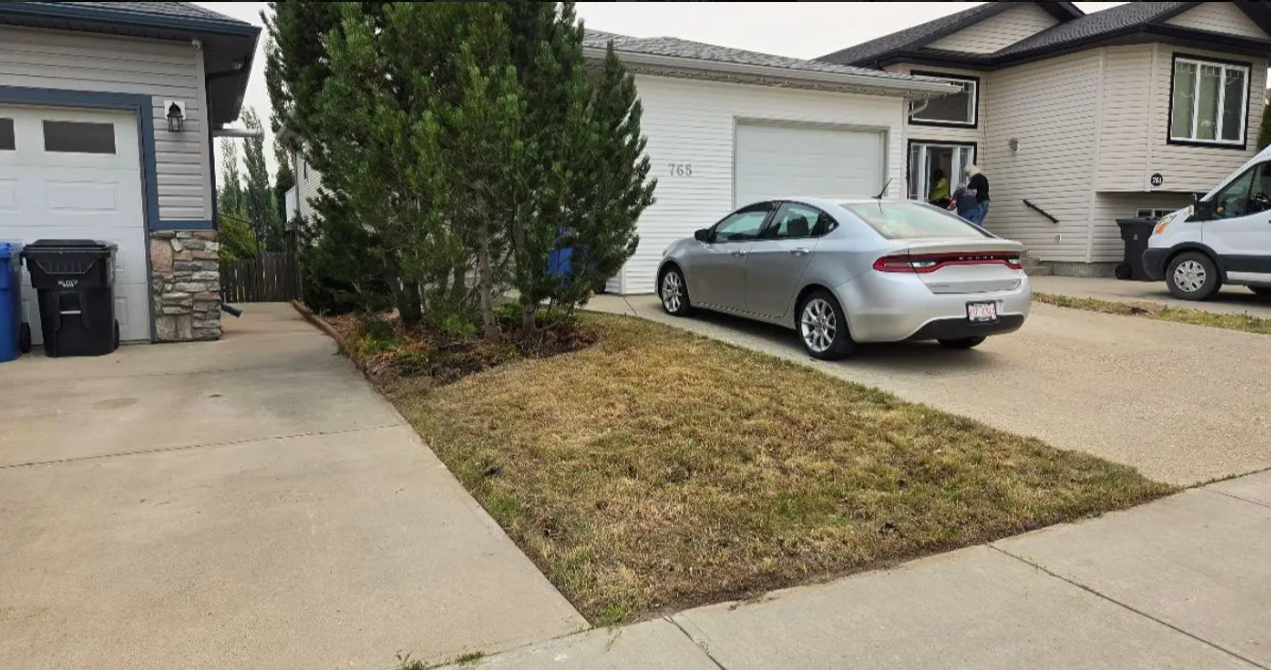 Suburban driveway with a silver sedan parked beside a small front yard and house