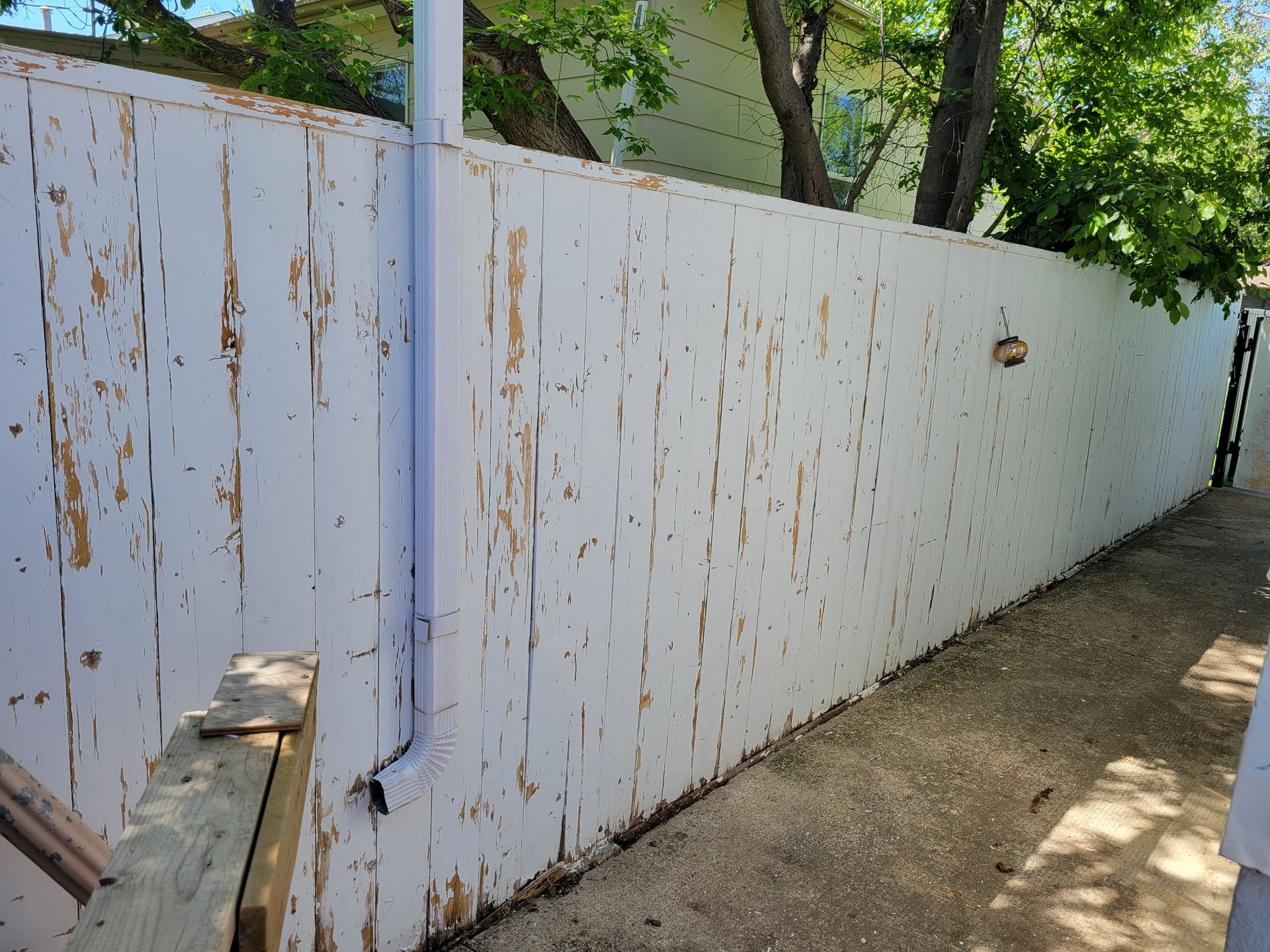 White wooden fence with peeling paint along a dirt path, trees visible above it