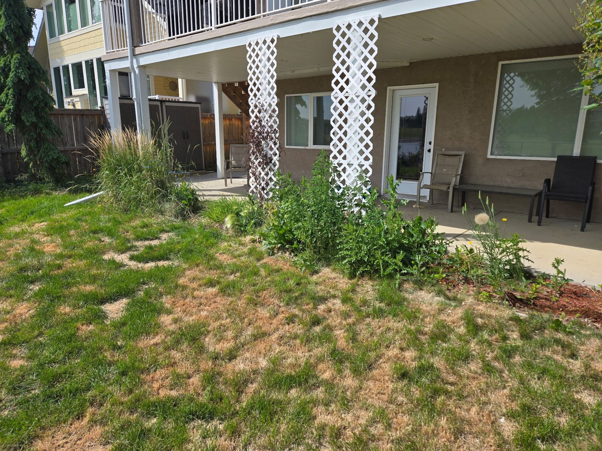 Apartment building patio with white railings, patio furniture, and a patchy grassy yard with weeds