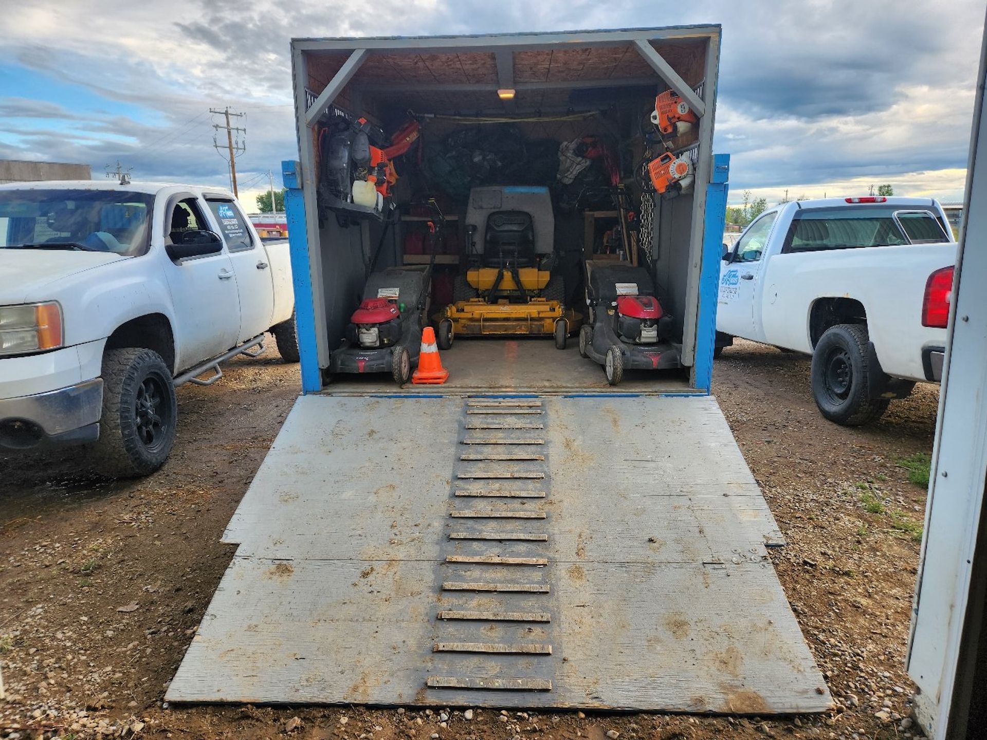 A landscape trailer with the rear ramp lowered, revealing lawn mowers and equipment.