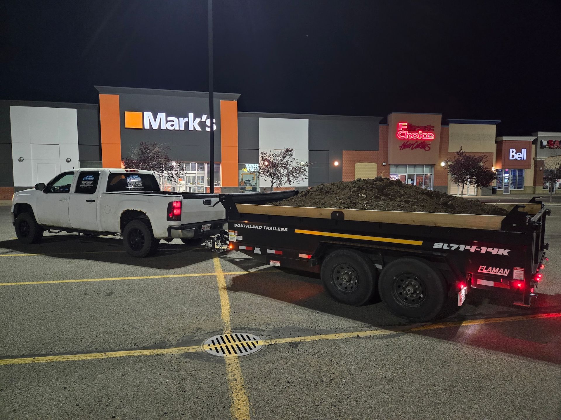 A white pickup truck pulling a black dump trailer filled with mulch.
