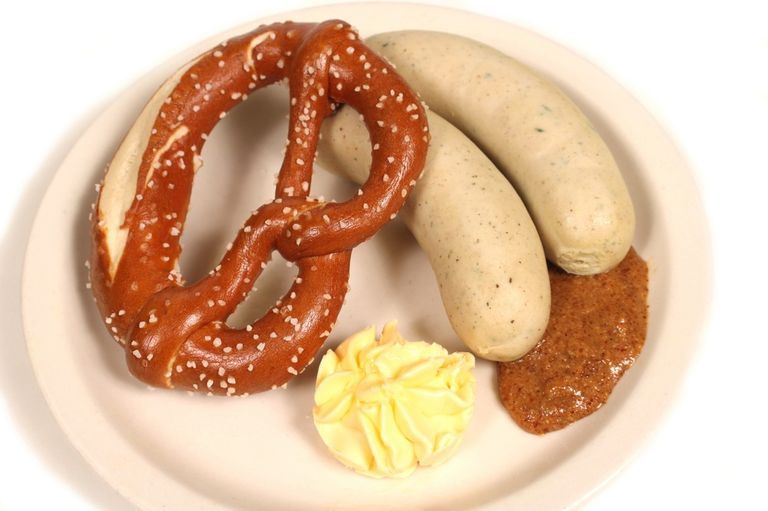 Pretzel, two white sausages, mustard, and butter on a plate.