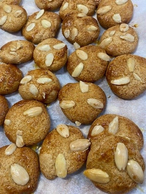 Golden-brown cookies, topped with almond slivers, arranged on a white surface.