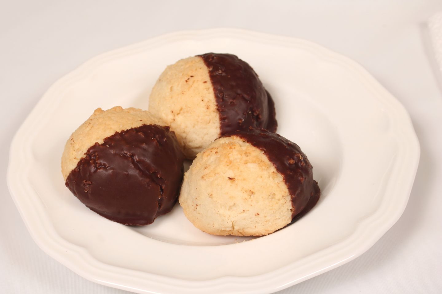 Three coconut macaroons dipped in dark chocolate on a white plate.
