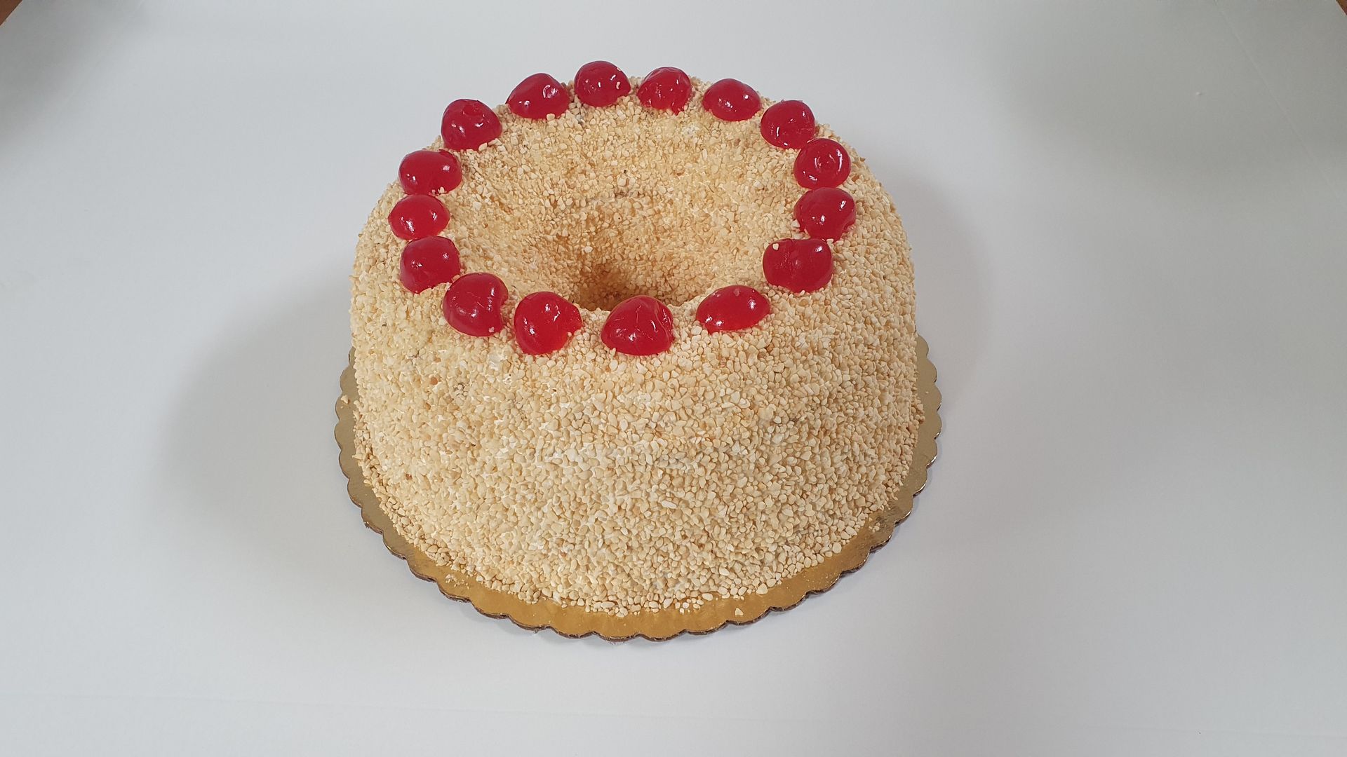 Angel food cake with small sprinkles, topped with red cherries on a white surface.