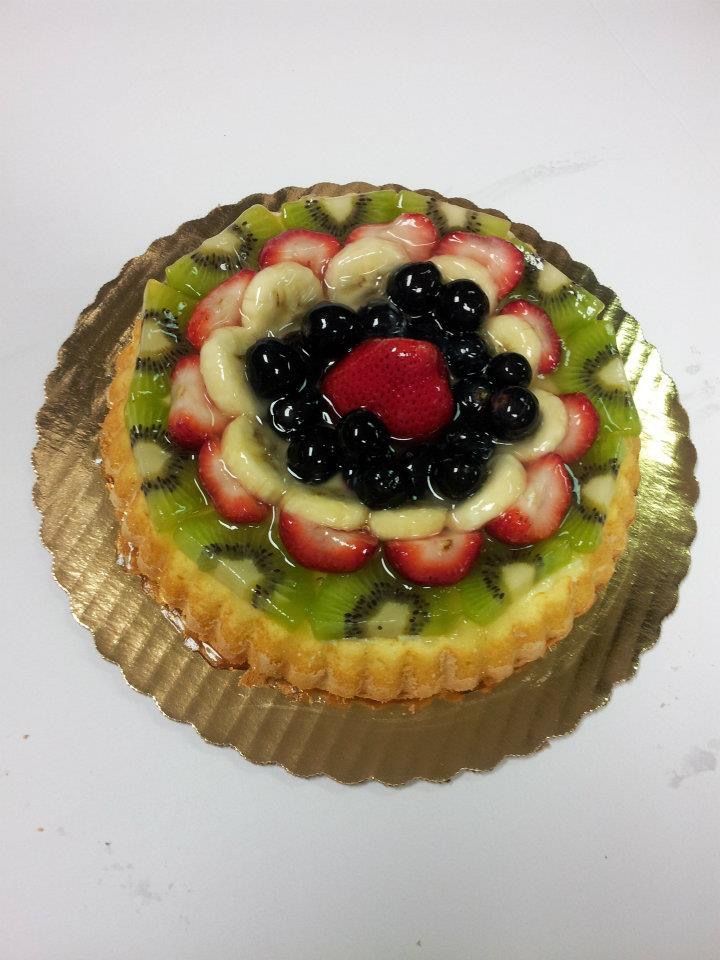 Fruit tart with kiwi, strawberries, blueberries, and bananas on a gold paper doily.