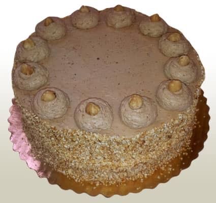 Cake with brown frosting, hazelnut topping, and nut-covered sides, sitting on a gold-colored plate.
