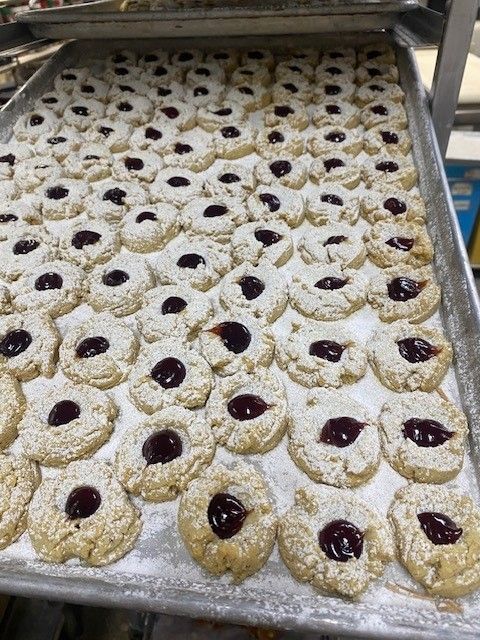 Sheet pan of thumbprint cookies dusted with powdered sugar and filled with jam.