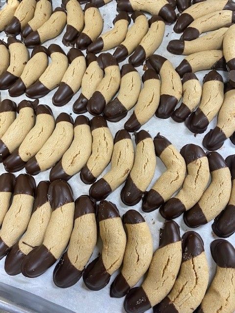 Rows of peanut-shaped cookies, dipped in chocolate, on a white surface.