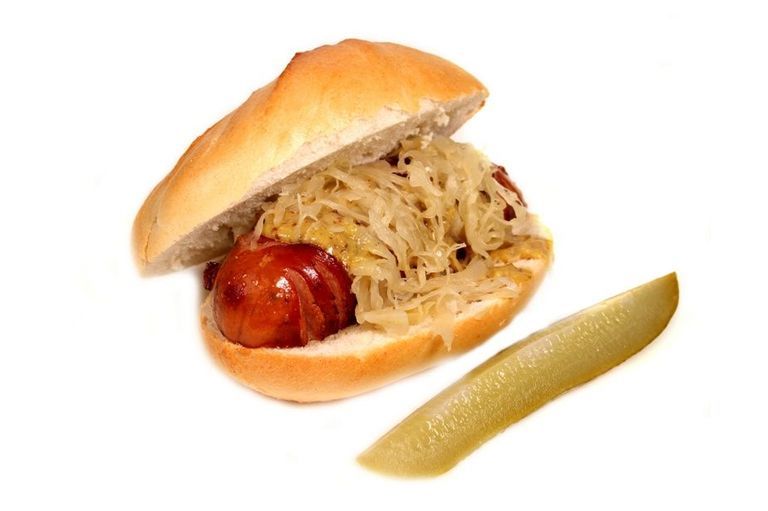 Hot dog in bun with sauerkraut and pickle slice.