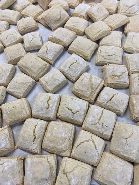 Square-shaped, light-brown biscuits arranged on a flat surface, some showing cracked surfaces.
