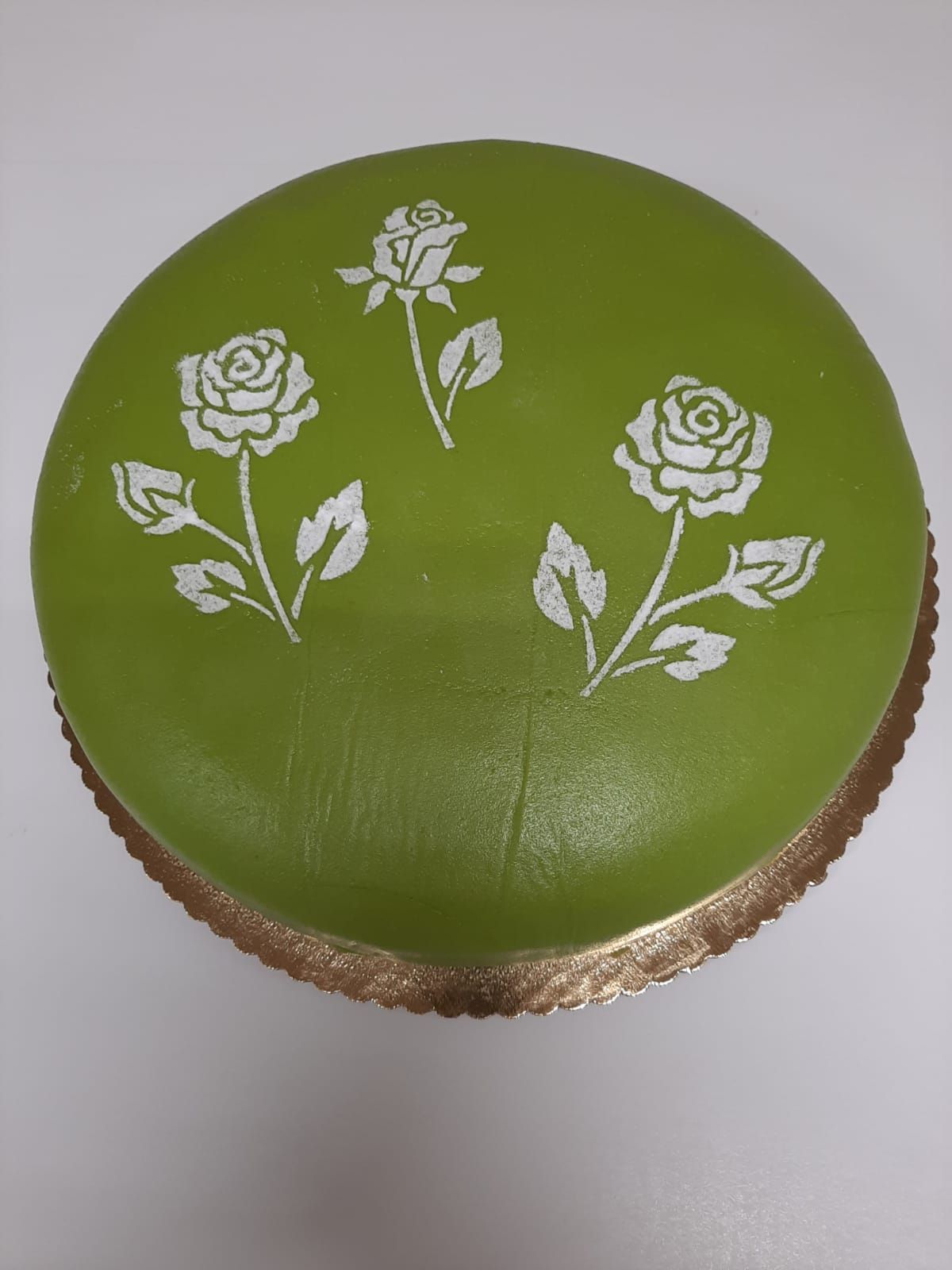 Green cake with white rose design on a gold cake board.