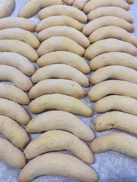Rows of crescent-shaped, pale yellow cookies on parchment paper.