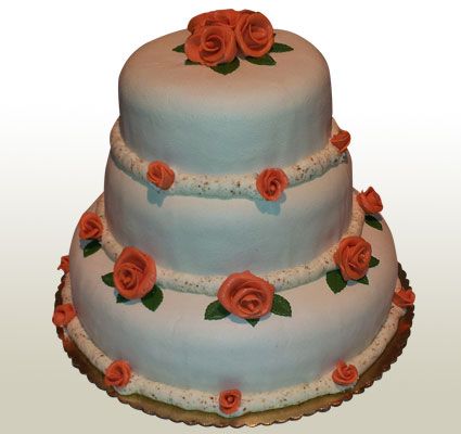 Three-tiered white cake with orange roses and green leaves, on a gold base.