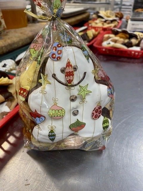 Snowman-shaped cookie, decorated with colorful ornaments, in a cellophane bag, sitting on a counter.