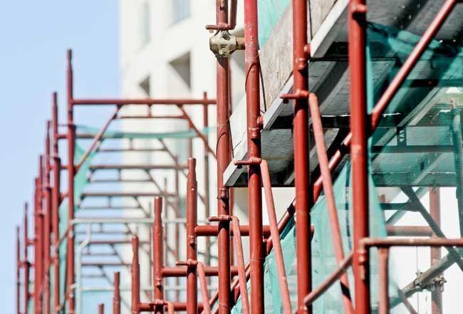 A Row Of Red Scaffolding Is Lined Up In Front Of A Building Under Construction — Triple S Scaffolding In Wauchope, NSW