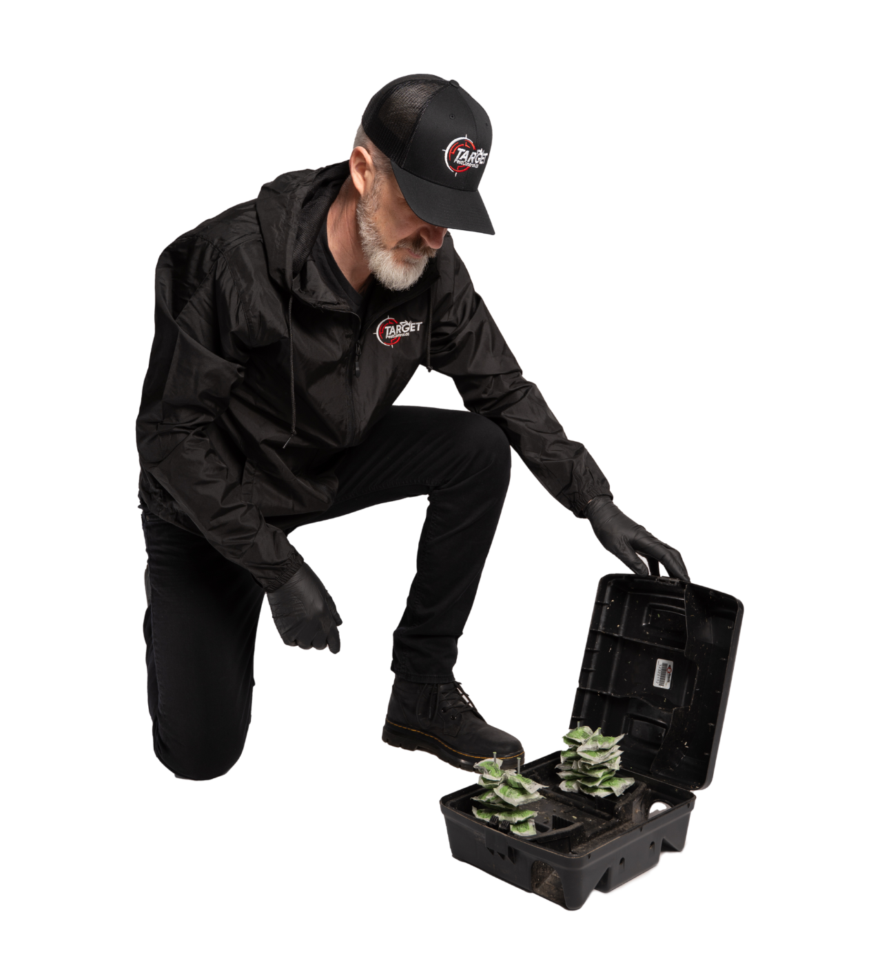 A man in a black hat is kneeling down next to a box with mouse bait in it.