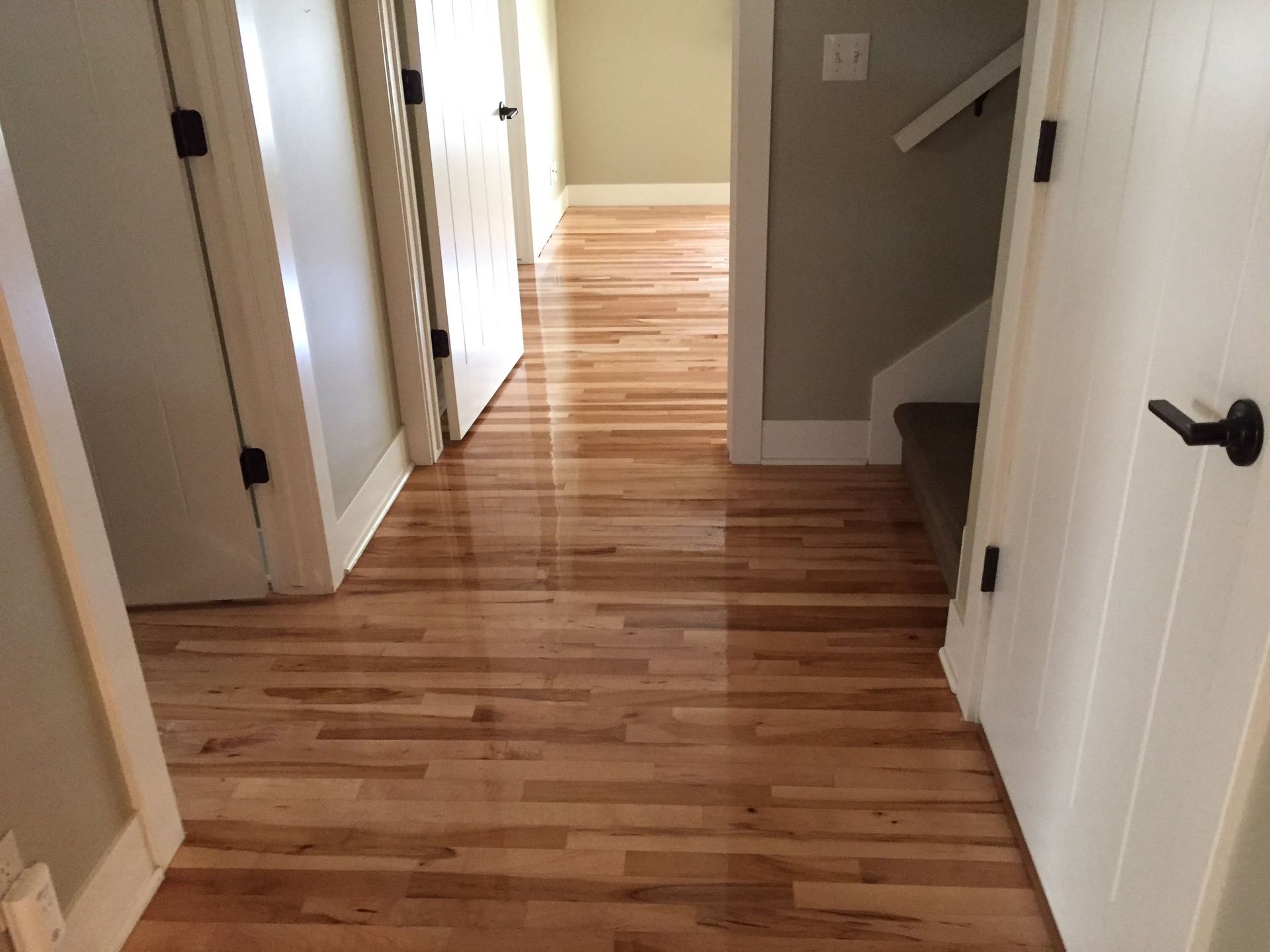 Wooden hallway with white doors and stairs leading to a brighter room.