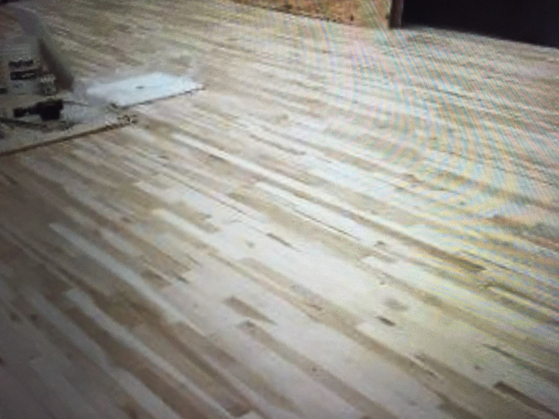 Wooden floorboards in a room, with a chair and papers in the upper left corner.