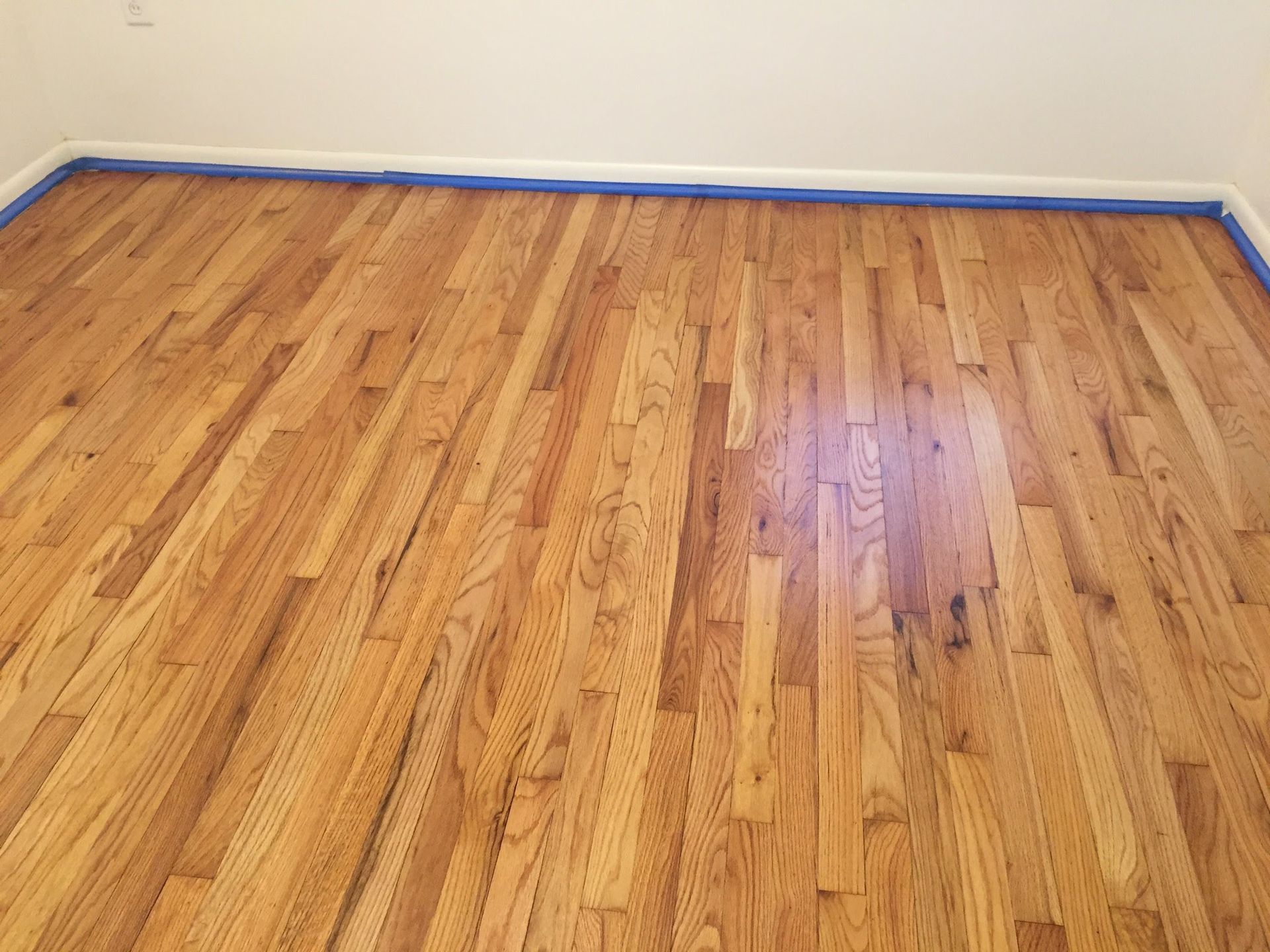 Empty room with a polished hardwood floor and blue painter’s tape along the walls