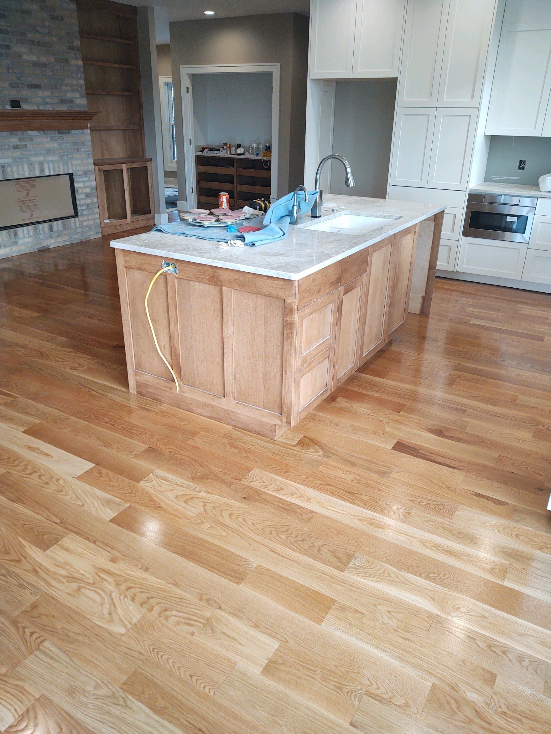 Empty kitchen with hardwood floors, a central wooden island, and a stone fireplace in the background