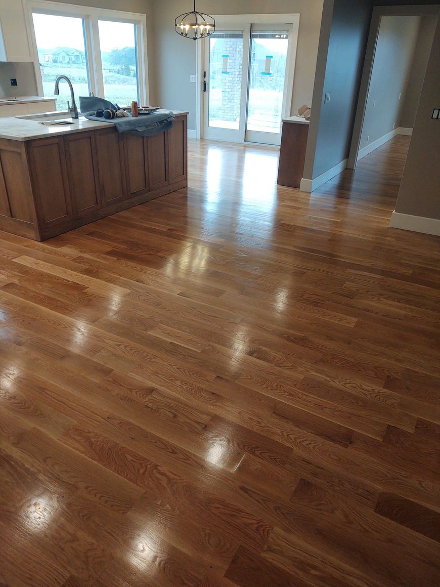 Empty hardwood-floored kitchen with island, pendant light, and sliding glass doors to a snowy deck.