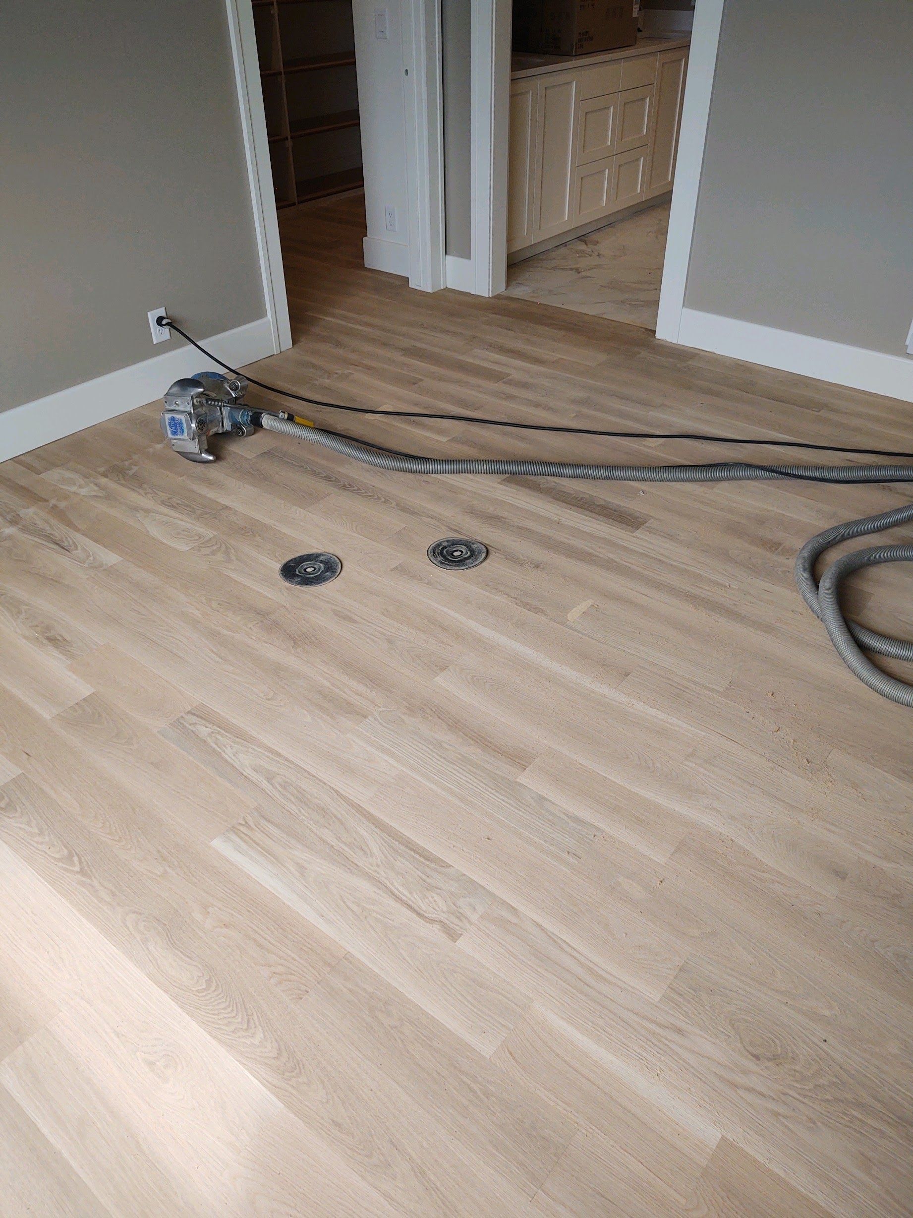 Cables and a power tool on a light wood floor near a doorway and carpeted room.