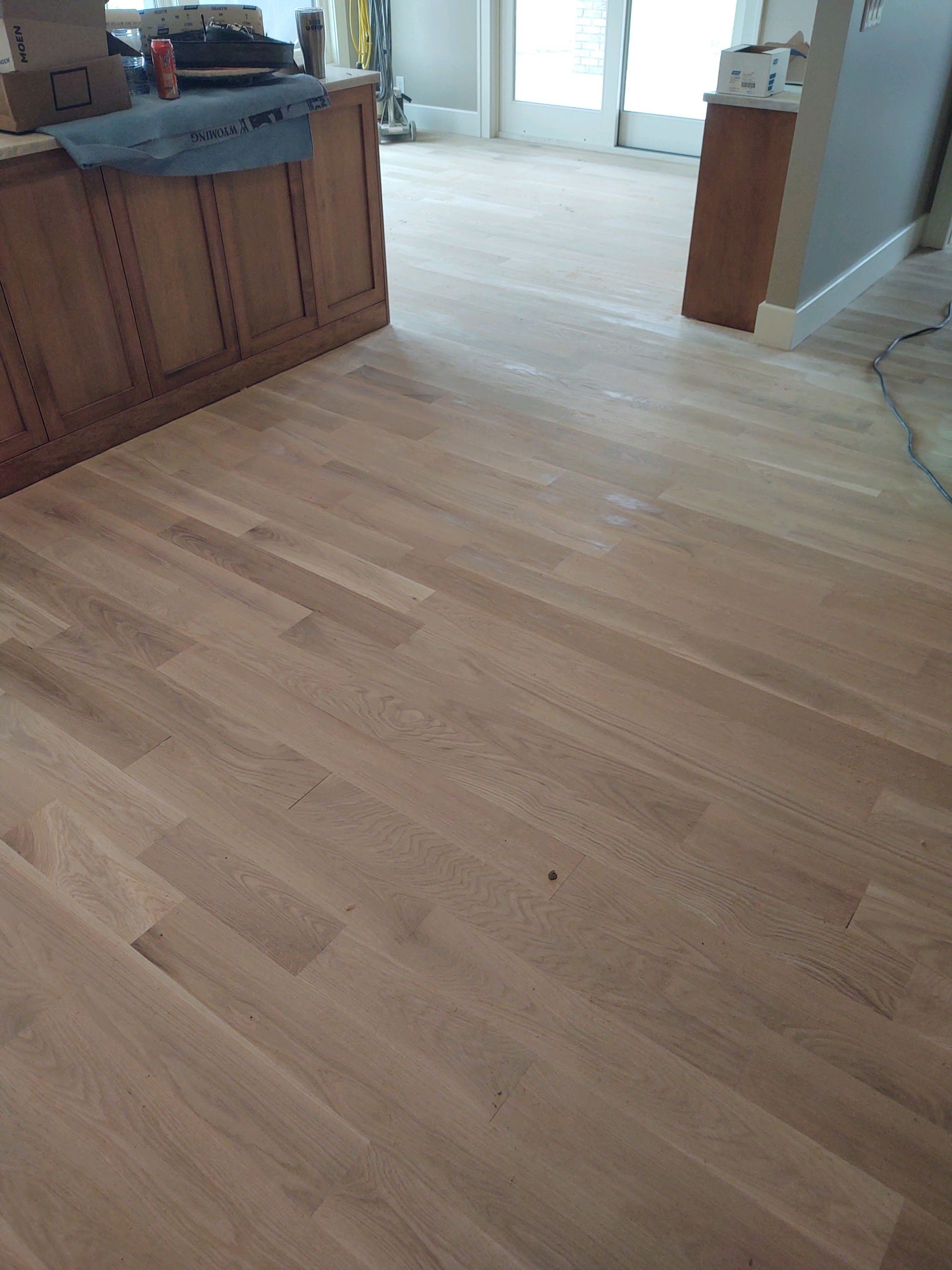 Empty wood-floored kitchen with cabinets and a doorway to another room.