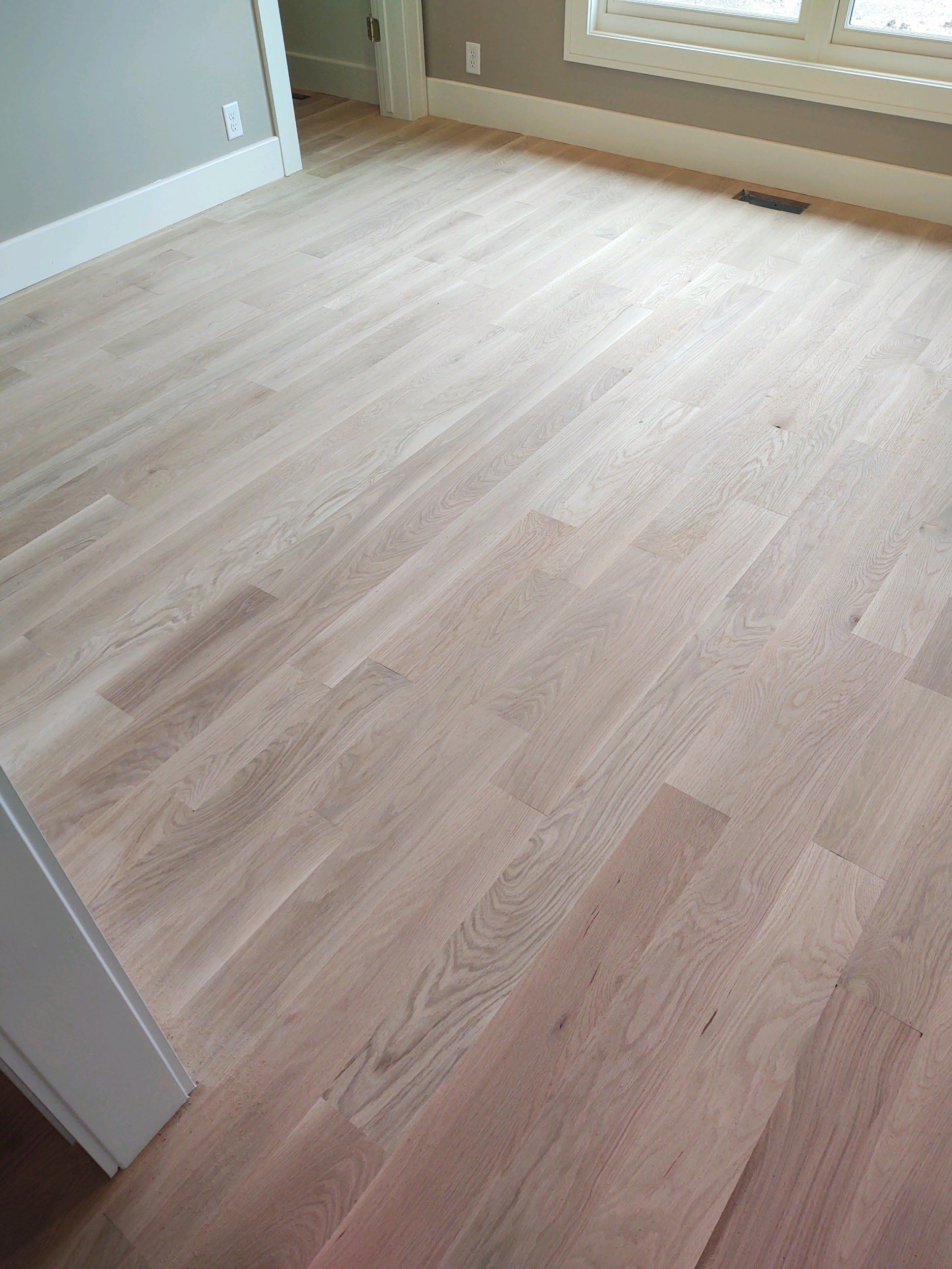 Empty light wood-floored room with pale walls and a window seat.