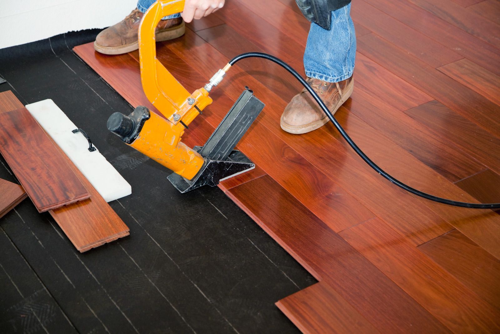 Installing black underlayment and wood flooring with a yellow floor stapler on a hardwood floor