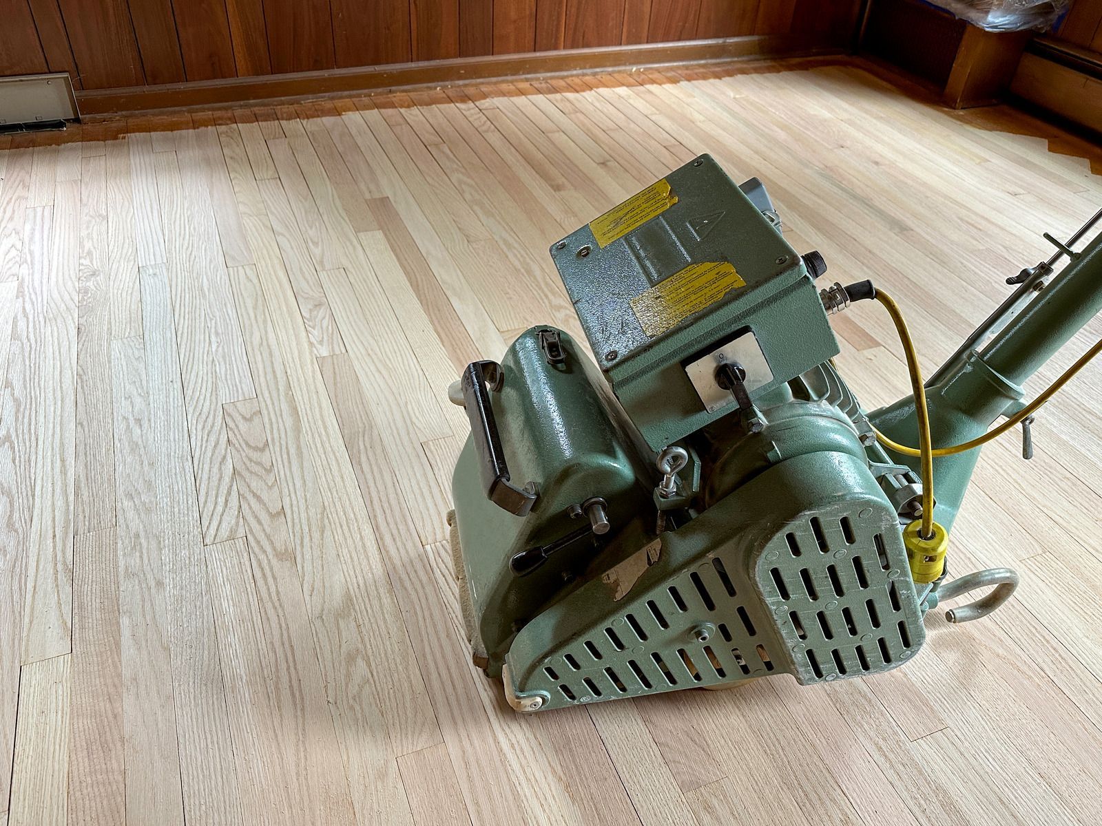 Floor sander on a wooden floor with a green motor and metal dust guard