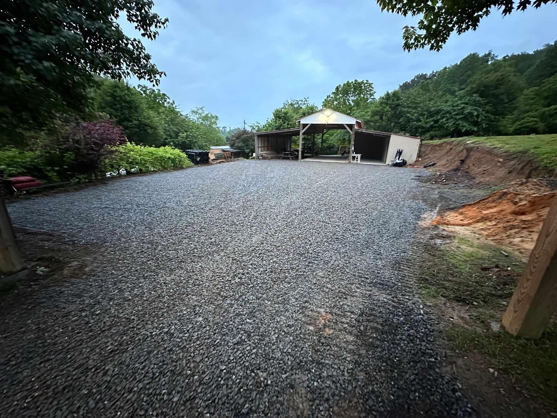 A wide, gravel-covered driveway leading toward a wooden shed structure under a cloudy sky.
