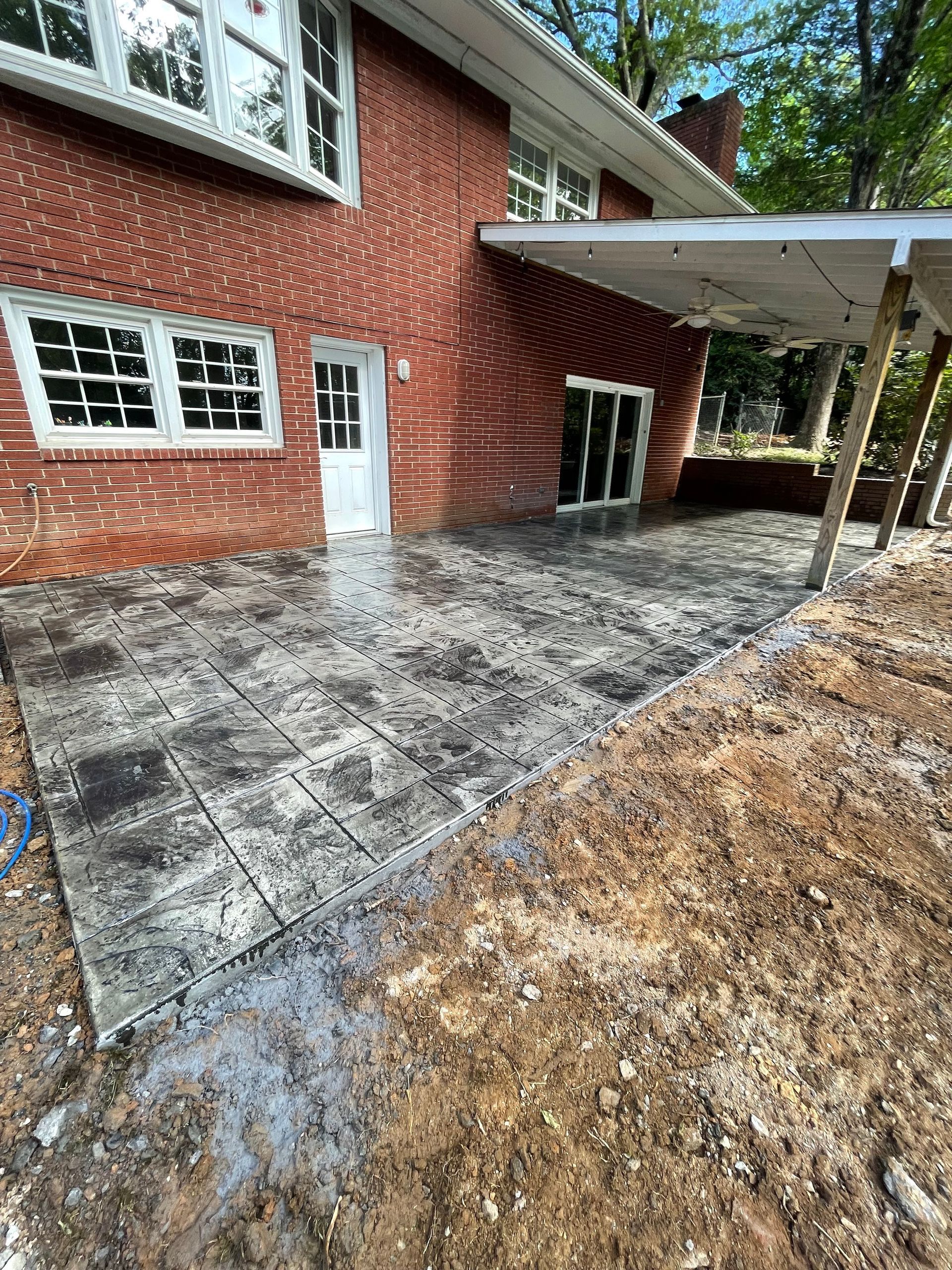 A freshly poured stamped concrete patio in front of a red brick house with a covered porch.