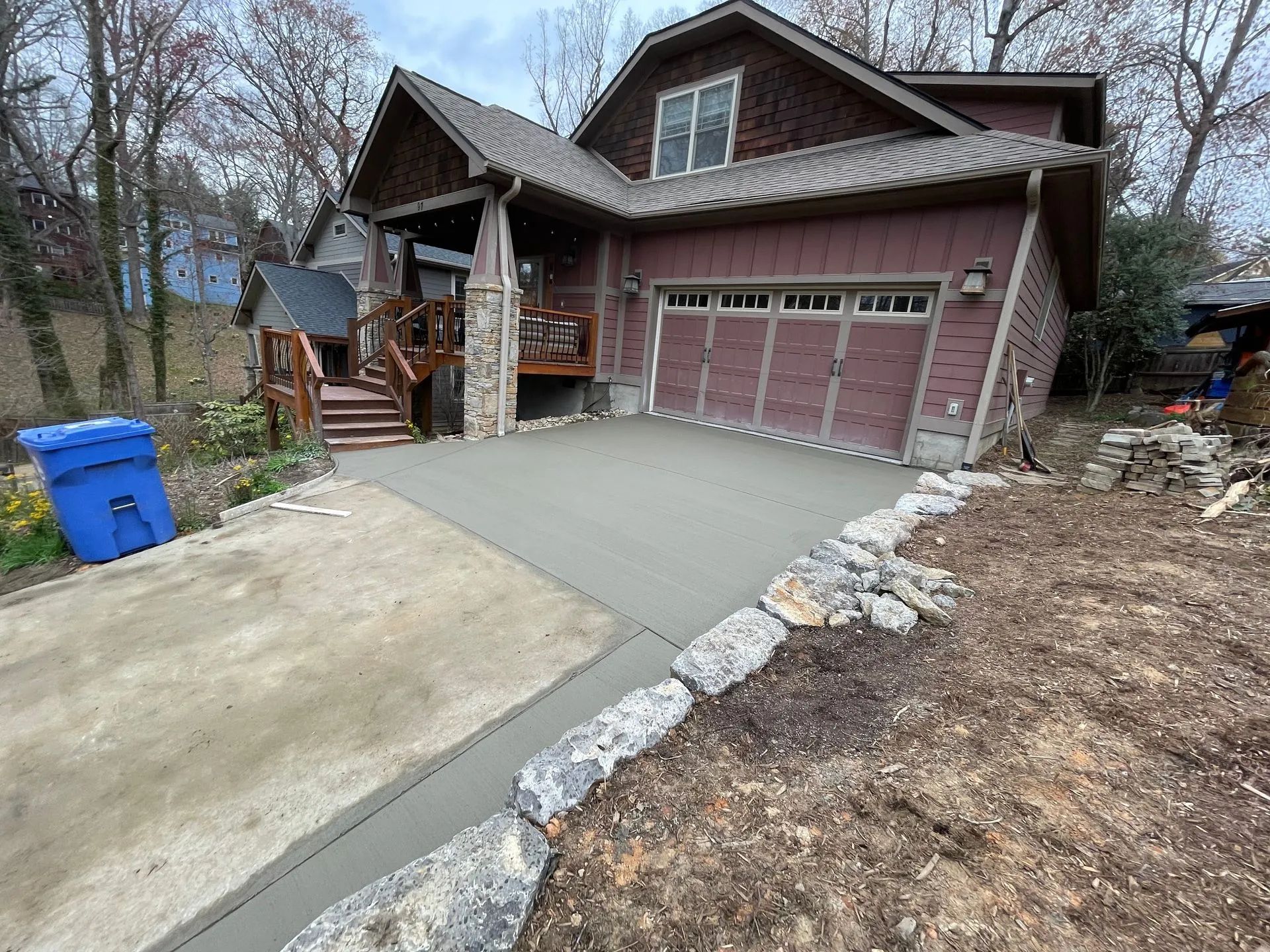 Driveway and garage of a house with fresh concrete and a stone border beside a sloped yard.