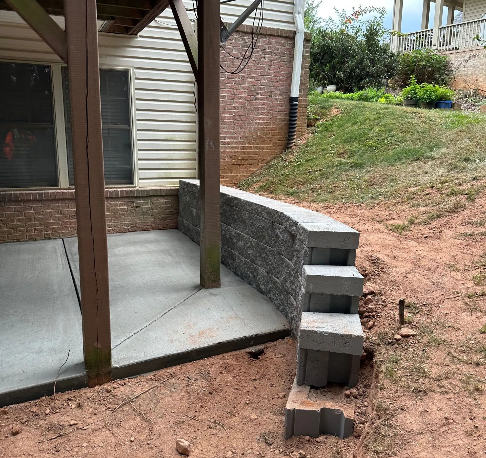 Backyard concrete stairs leading to a covered patio beside a brick wall and dirt slope
