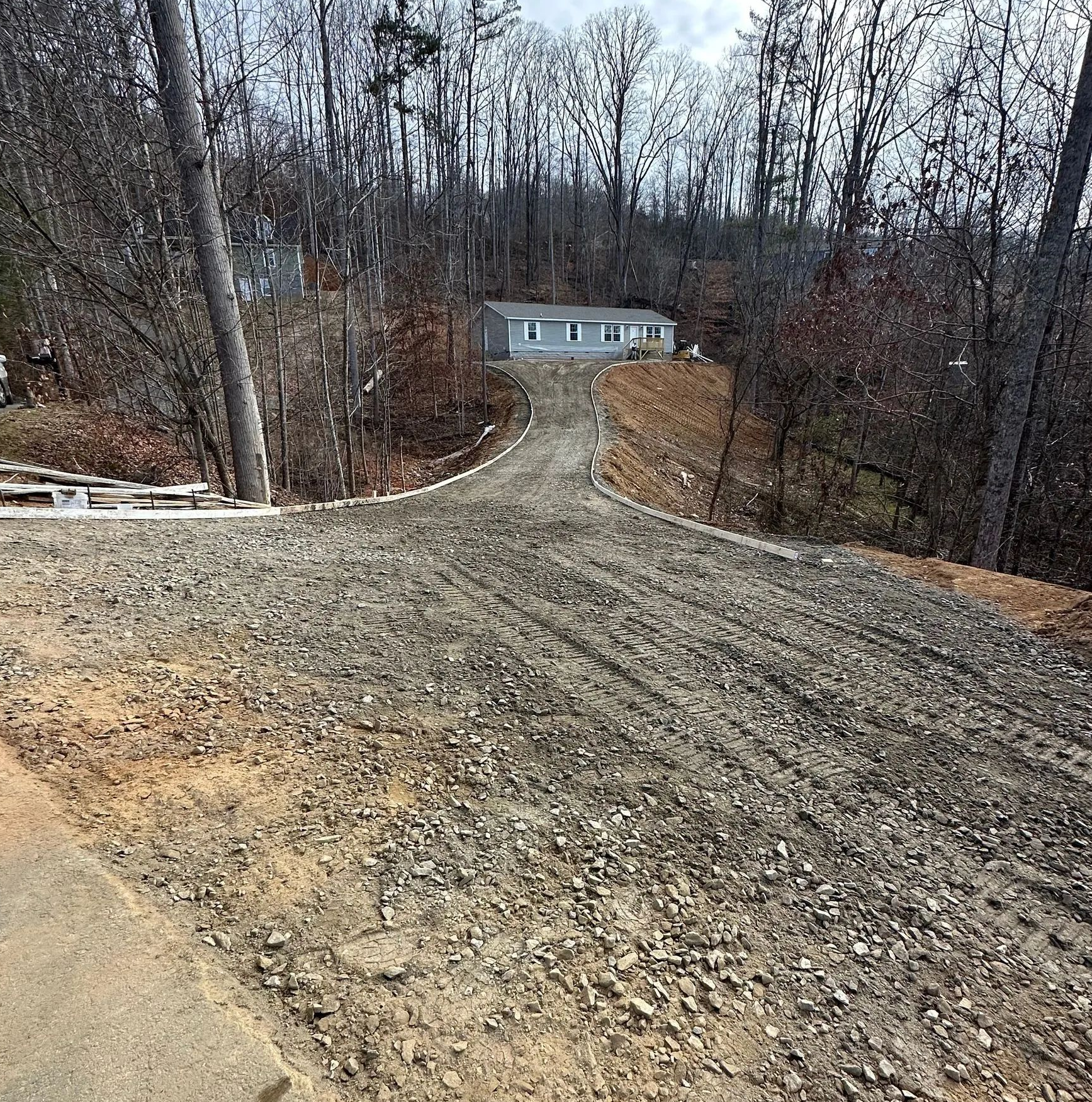 Gravel driveway on a wooded hillside leading to a small gray house in the distance