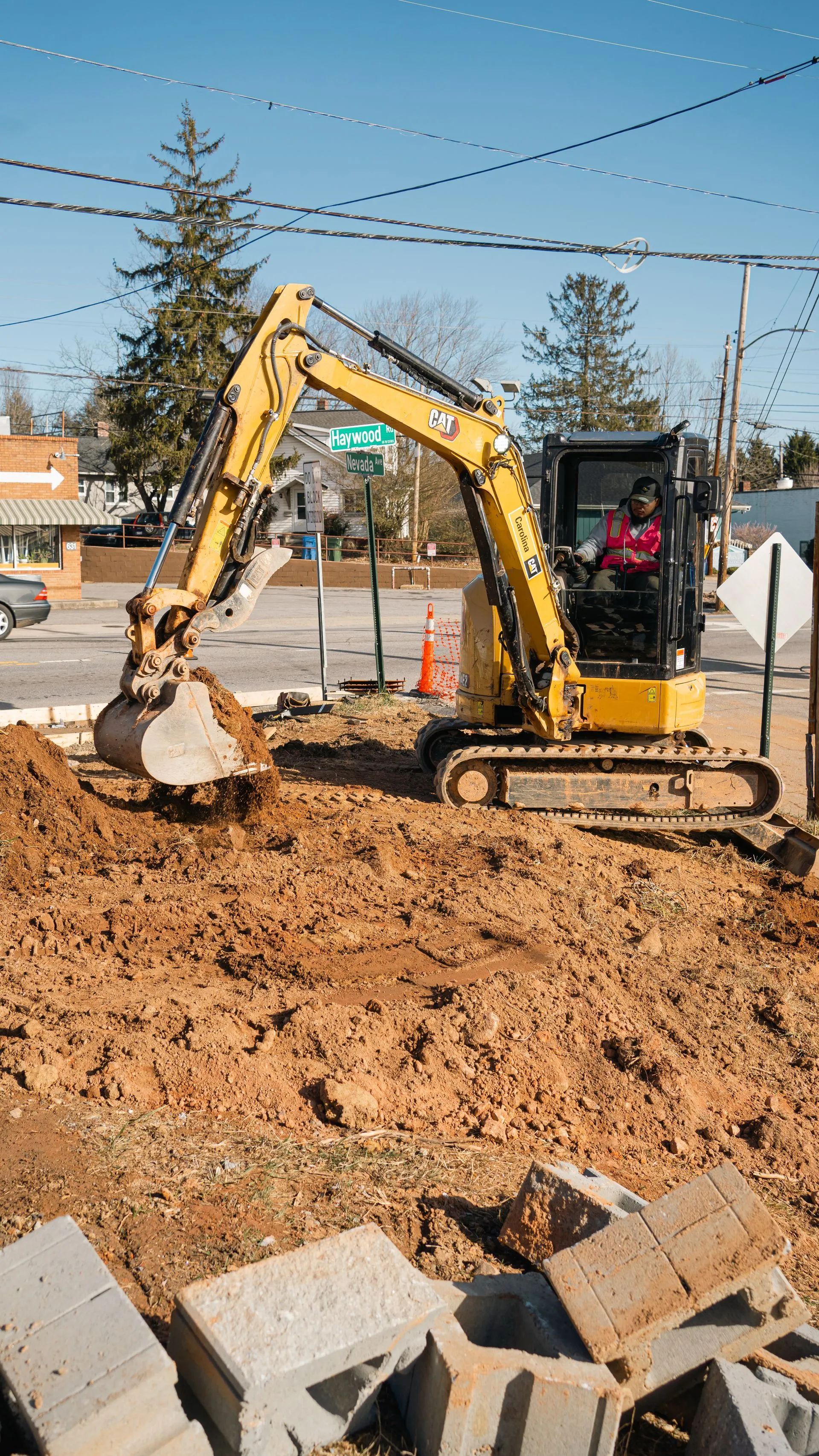 Yellow excavator digging dirt at a construction site with cinder blocks in the foreground