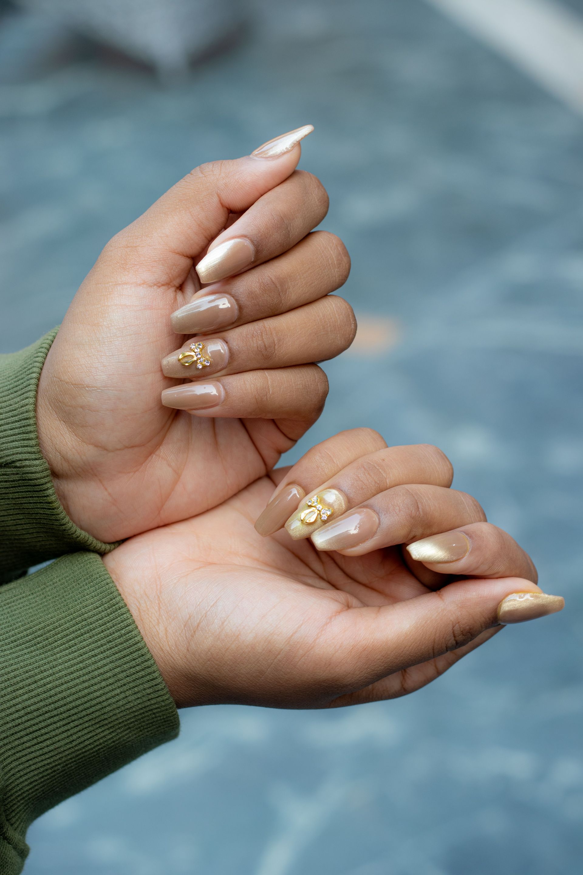 Two hands with gold glitter nail polish held together against a blue background